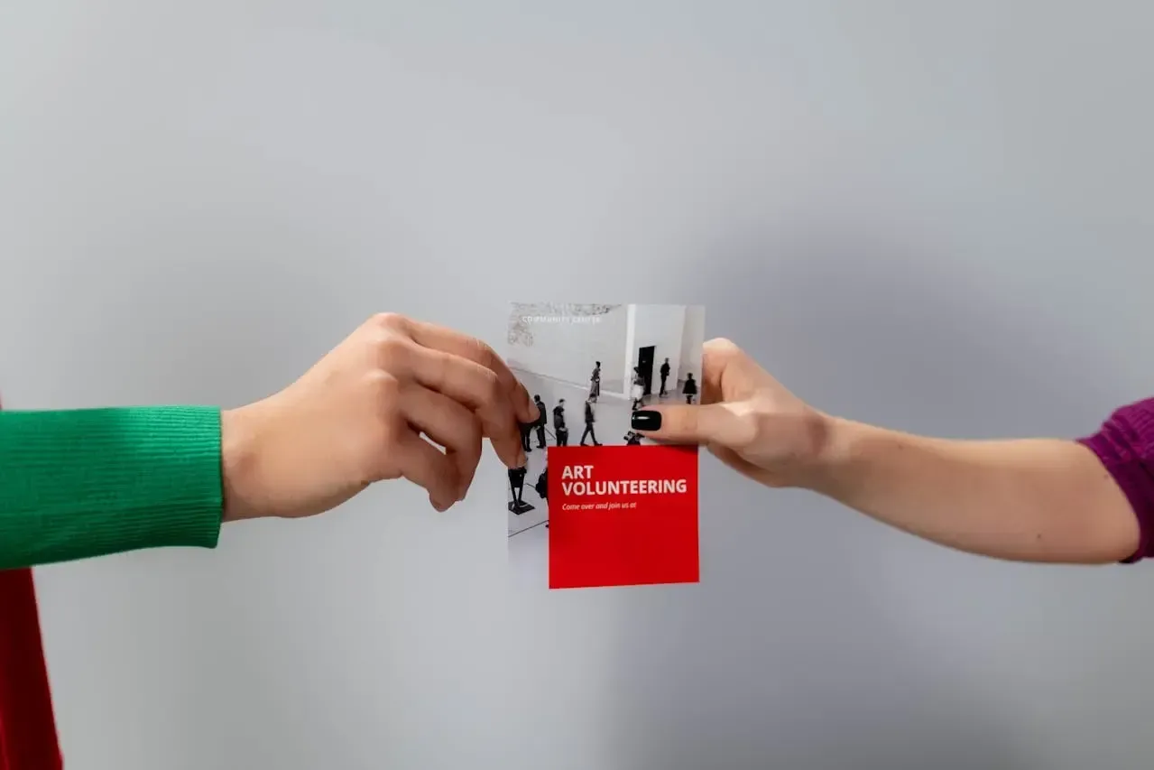 Dos personas intercambiando un flyer informativo con diseño en blanco, negro y rojo sobre actividades comunitarias.
