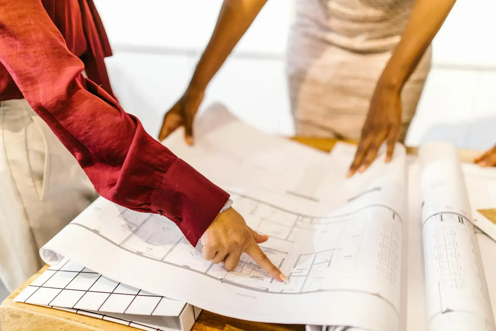 Dos personas revisando un plano arquitectónico sobre una mesa, señalando detalles del diseño.