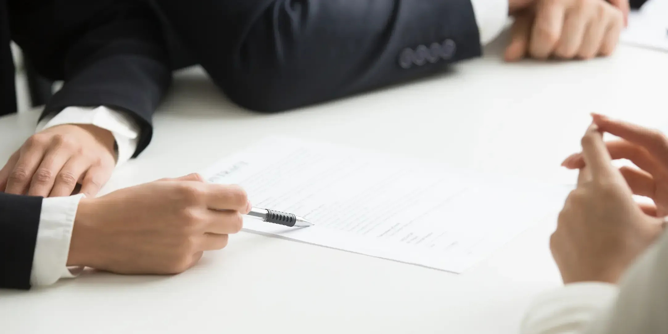 Grupo de personas en una mesa de trabajo revisando un documento, con una mano señalando el papel y otras participando en la conversación.